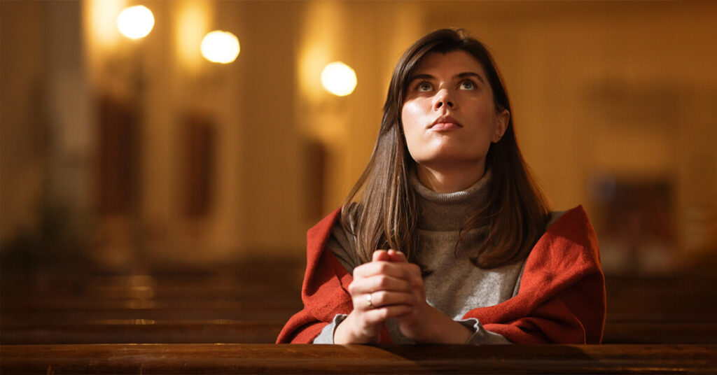 A young woman alone in a church, looking inward as sunlight shines through stained glass—representing Nicolette’s quiet and serious moment of reflection.